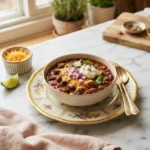 Bowl of thick pepperbellypete chili recipe topped with cheddar, onion, and sour cream